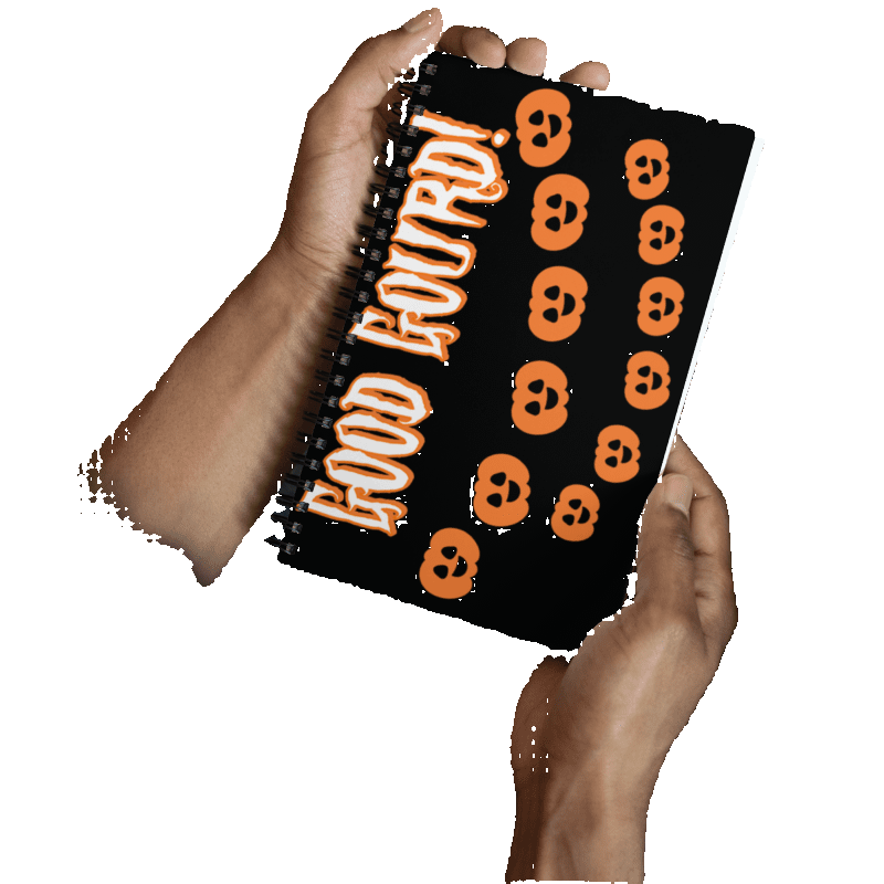 Person holding a notebook with Halloween-themed design featuring orange skulls and 'Good Boudri!' text.