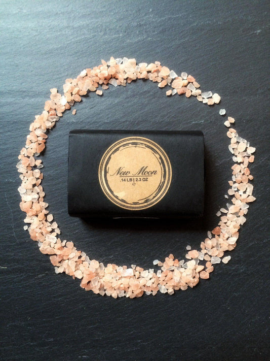 Black soap bar with gold label surrounded by small stones on a dark surface