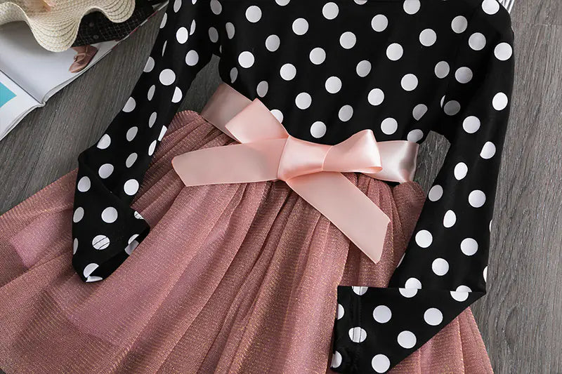 Black polka dot long-sleeve top with a pink bow on a pink skirt against a gray surface.