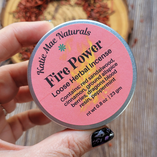 Katie Mae Naturals Fire Power loose herbal incense container held by a hand with black nail polish.