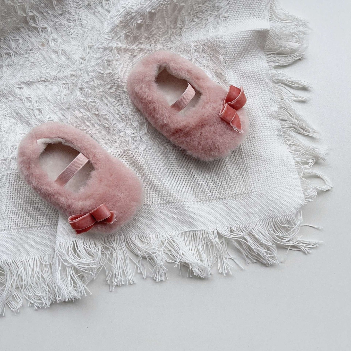 Pink fuzzy slippers with bow accents on a white textured blanket