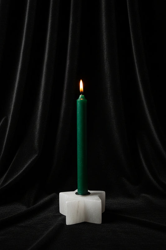 A green taper candle standing upright in a white star-shaped holder against a plain white background.