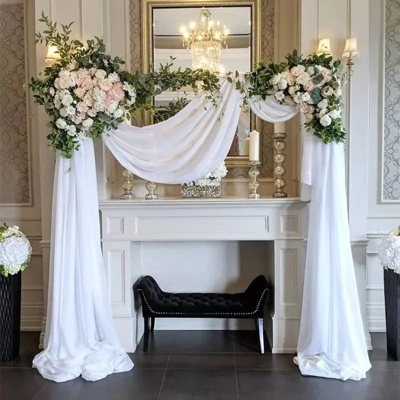 Decorative setup with flowers, white drapes, and candles in a room with a mirror and chandelier.