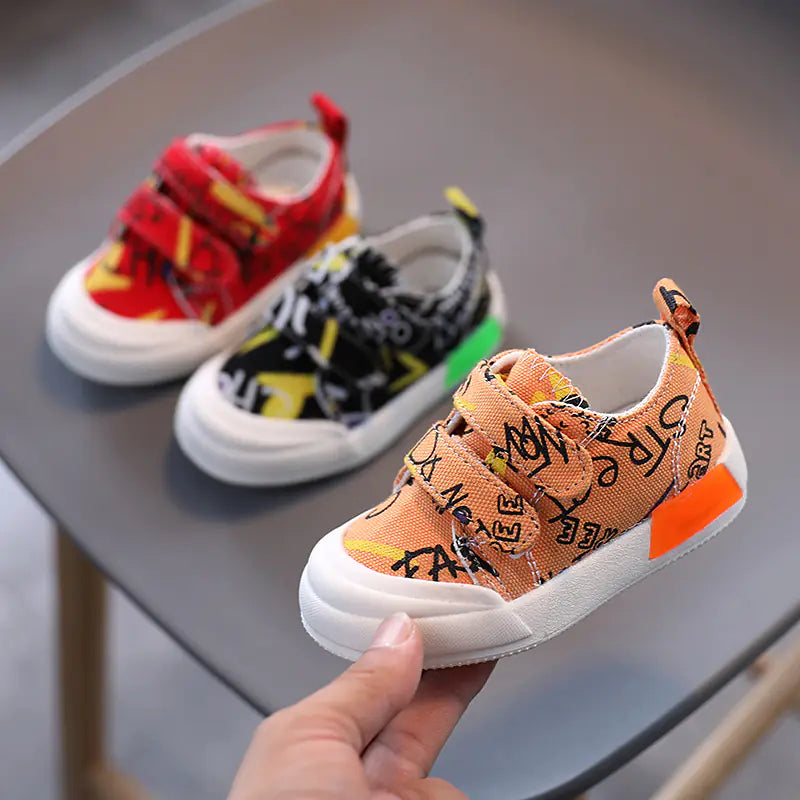 Colorful children's sneakers on a gray surface with one shoe held by a hand.