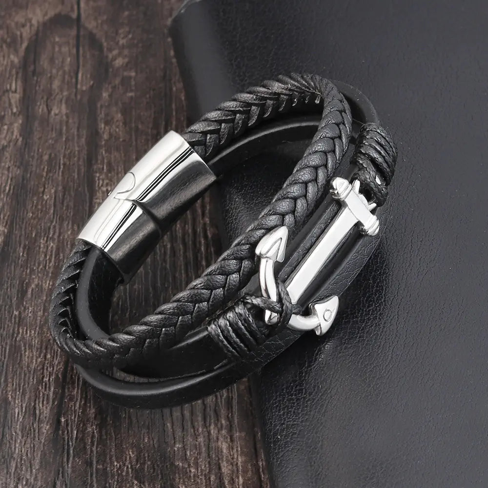 Black braided leather bracelet with silver anchor charm on a dark wooden surface