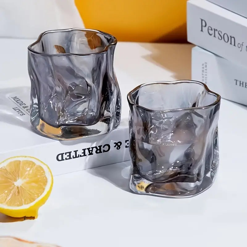 Two clear glass shot glasses on a white surface with a lemon wedge and a book in the background.