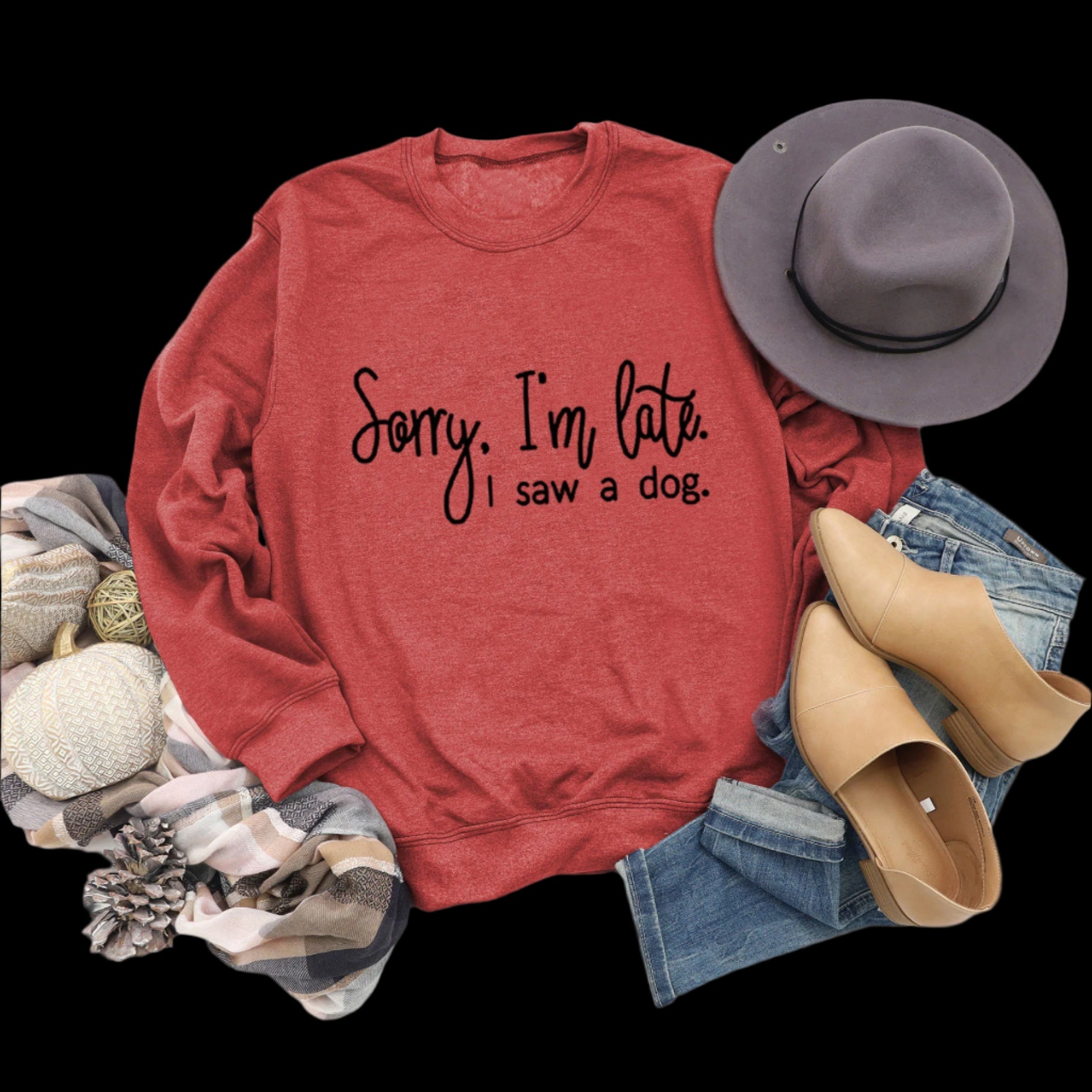 Red sweatshirt with text, hat, boots, and jeans on a wooden surface