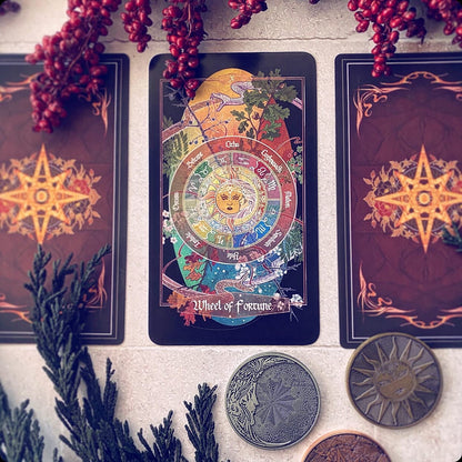 A tarot card deck displayed on a light stone surface, featuring the 'Wheel of Fortune' card in the center with two matching cards behind it. The cards have a dark reddish-brown background with gold starburst designs.