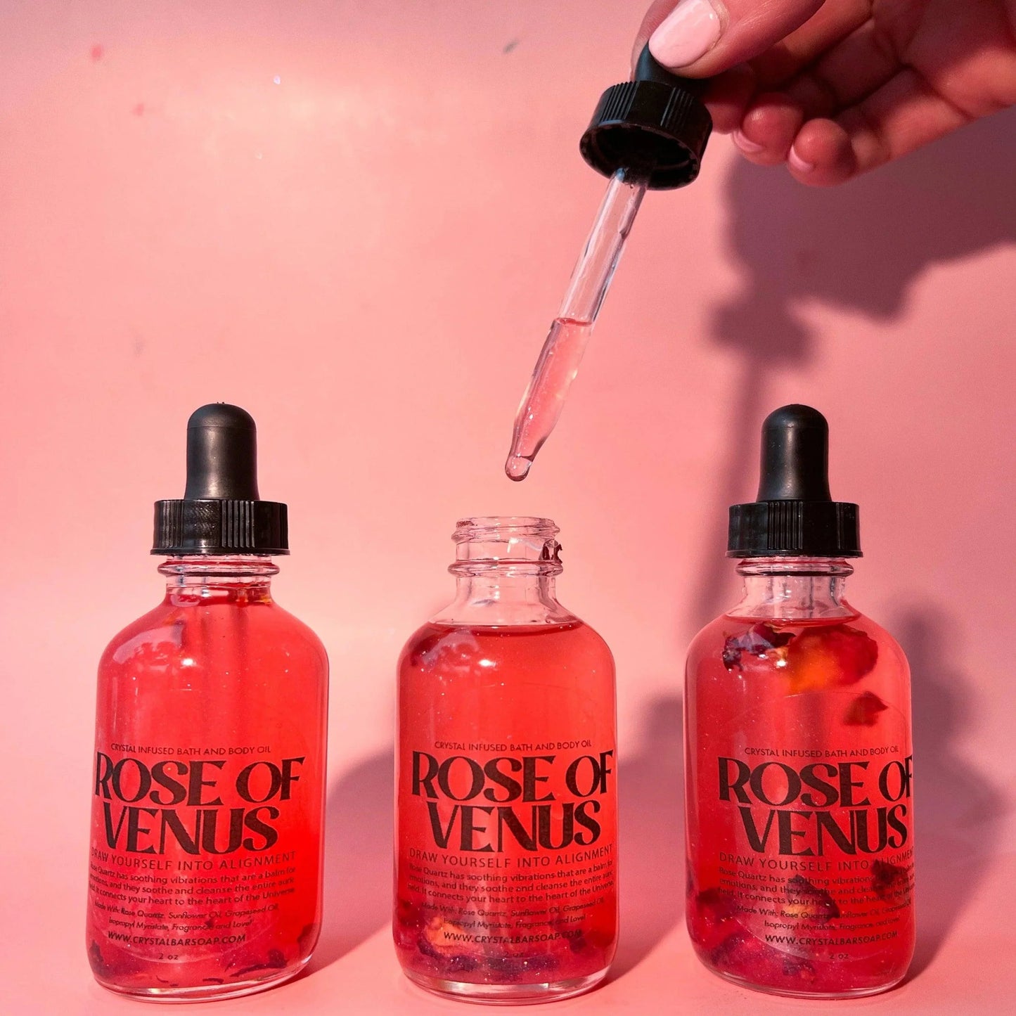 Three 'Rose of Venus' bottles with a dropper on a pink background