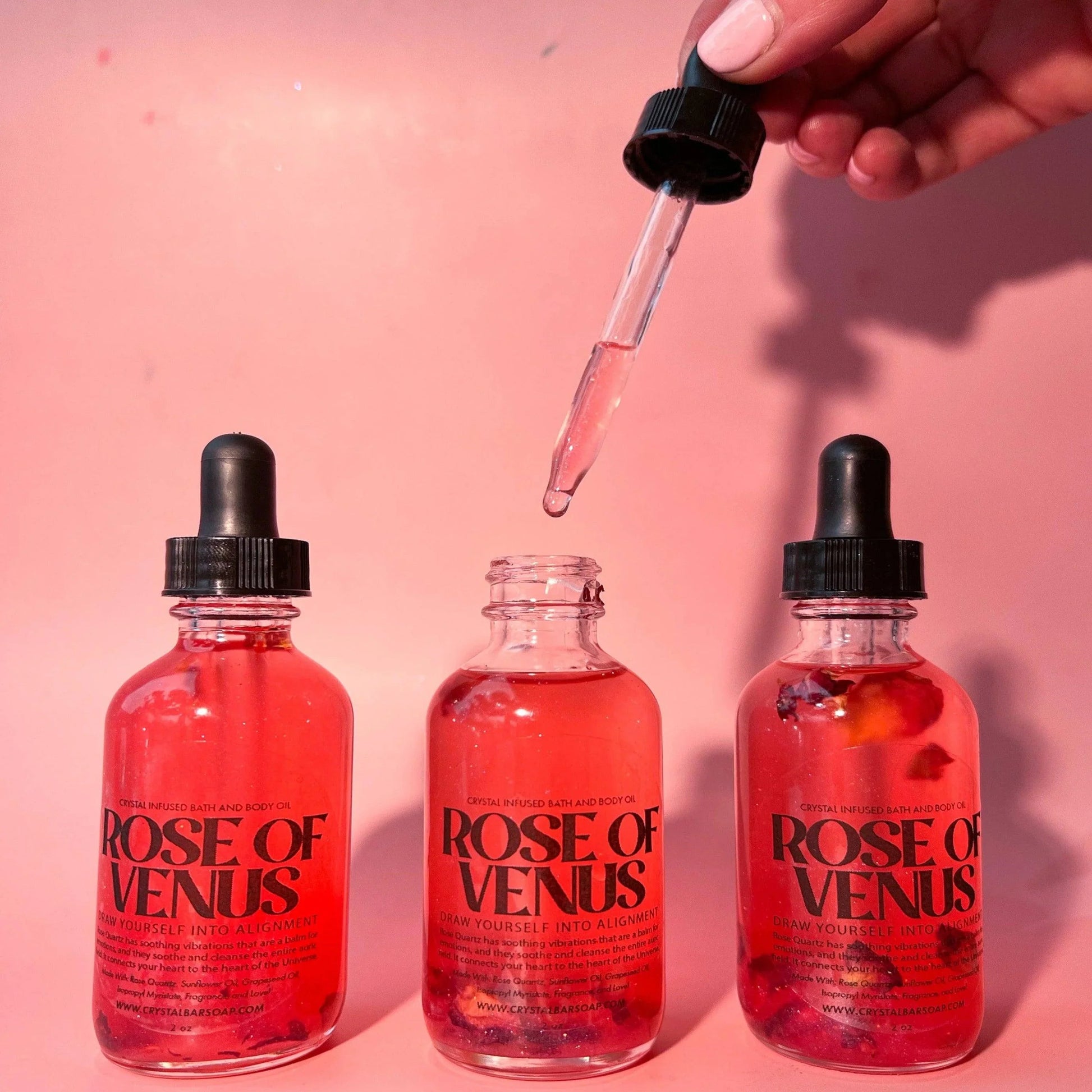 Three 'Rose of Venus' bottles with a dropper on a pink background