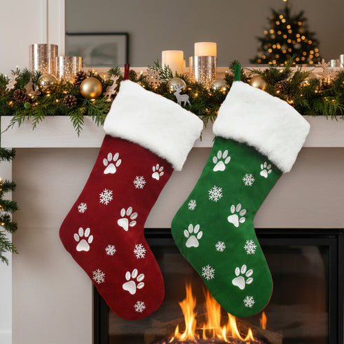 Red and green Christmas stockings with paw prints and snowflakes hanging by a fireplace.