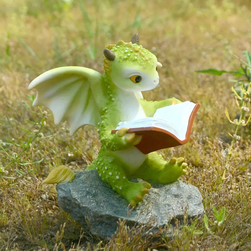 Green dragon figurine reading a book on a rock in a natural setting