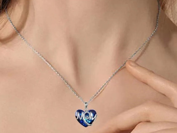 Necklace with a blue heart-shaped pendant featuring 'MOM' on a person's neck.