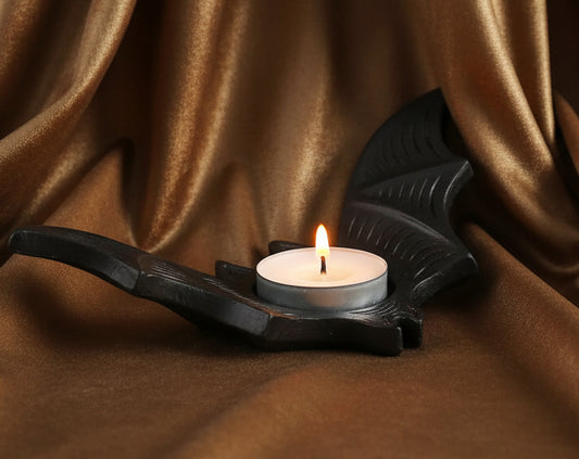 Black bat-shaped candle holder with a lit white candle on a white background