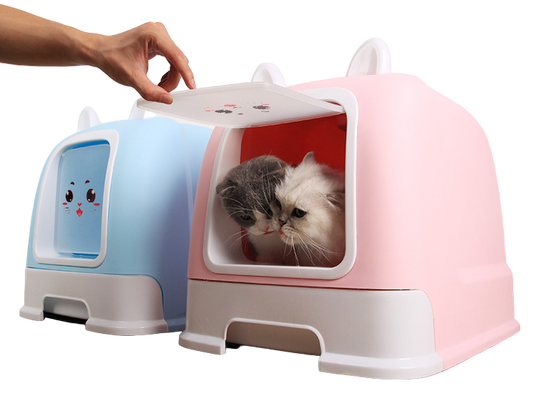 Pink pet litter box with a cat peeking out, next to a blue one on a wooden floor.