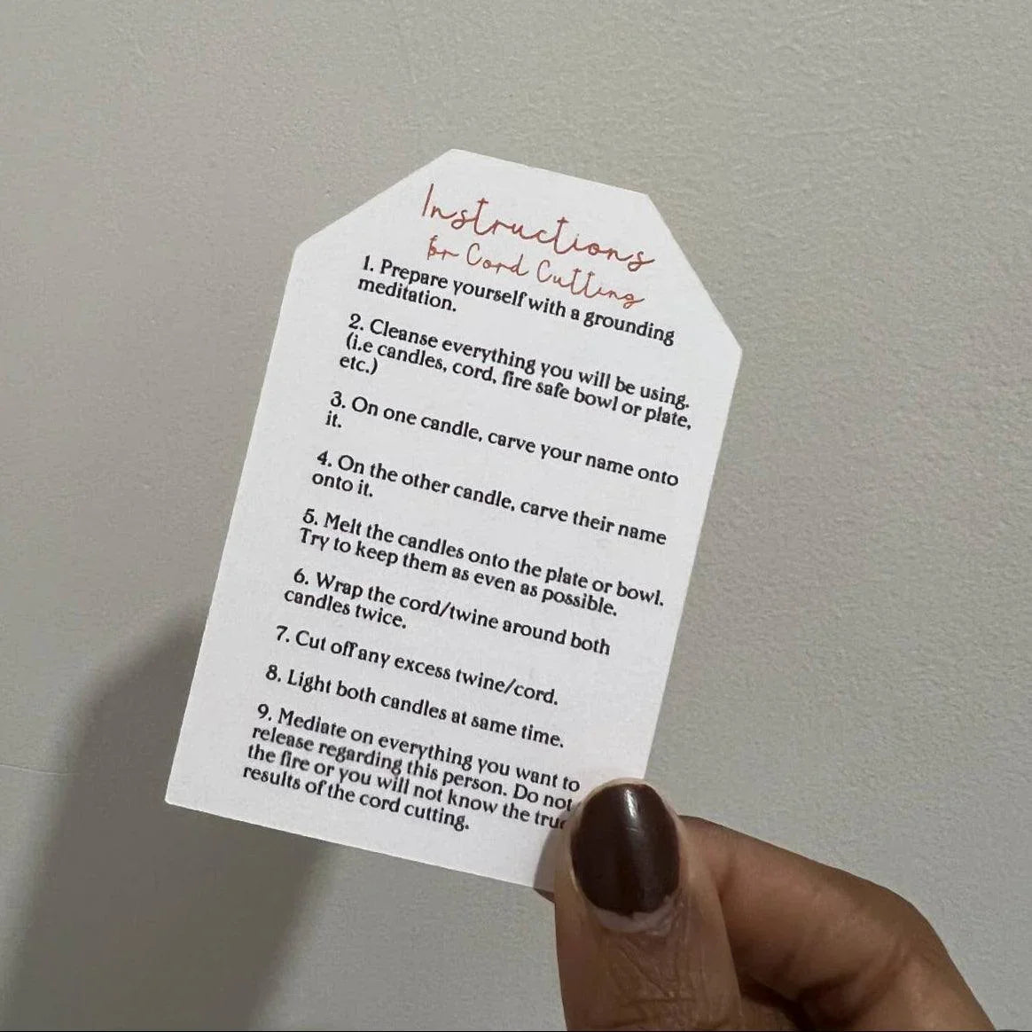 Hand holding a card with instructions for cord cutting meditation against a plain background