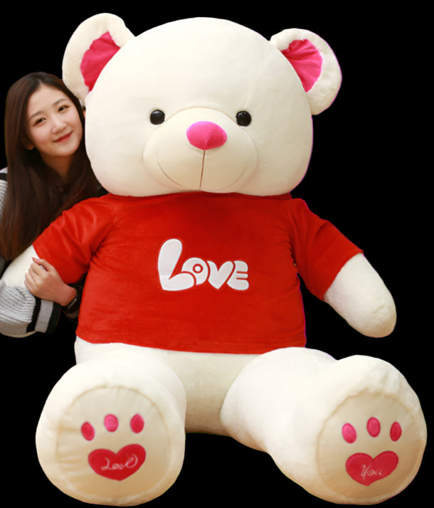 Woman sitting next to a large white teddy bear with a red 'LOVE' shirt in a room with bookshelves.