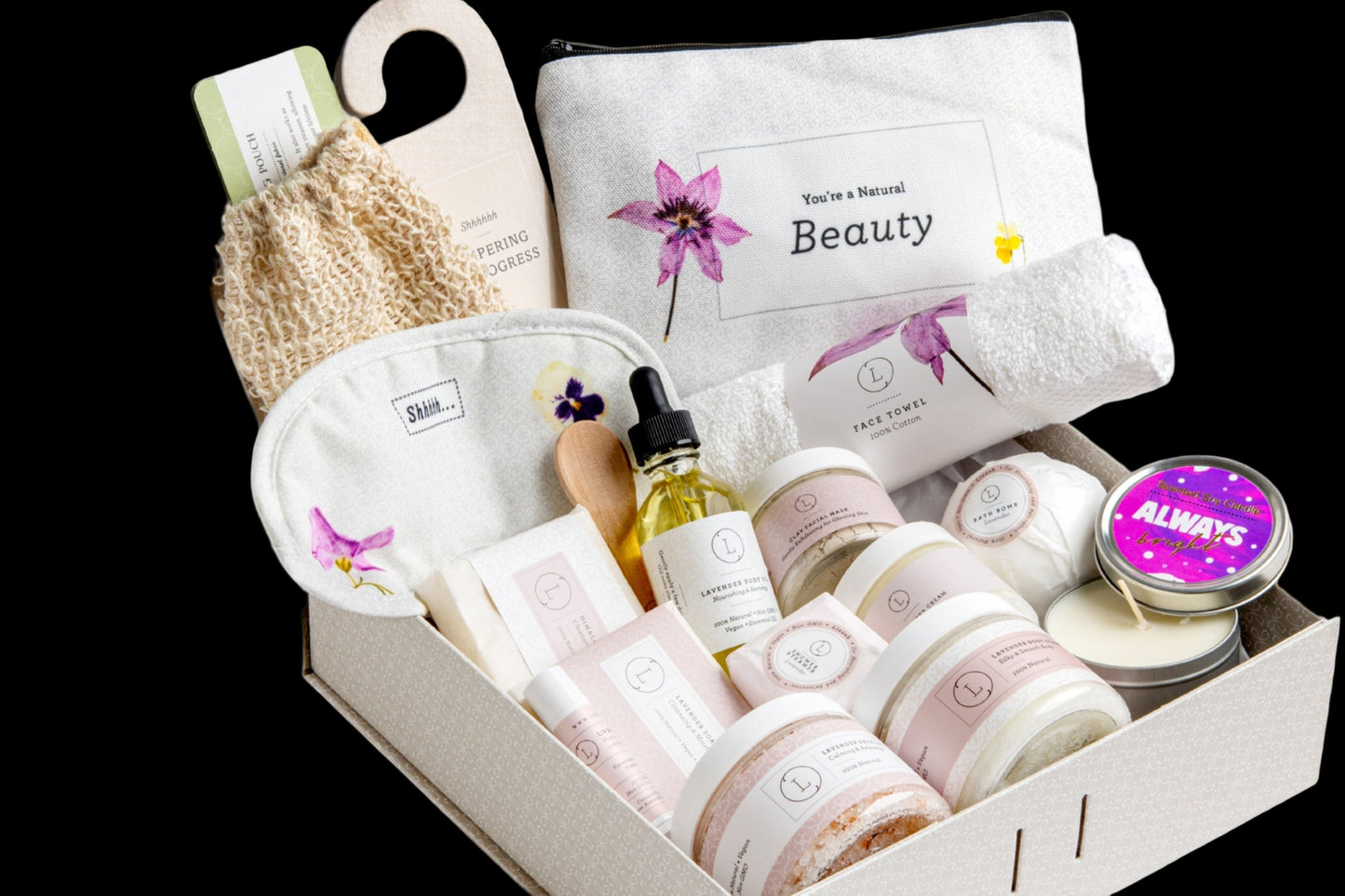 Gifting box with beauty products including candles, bottles, and a scrub on a white background