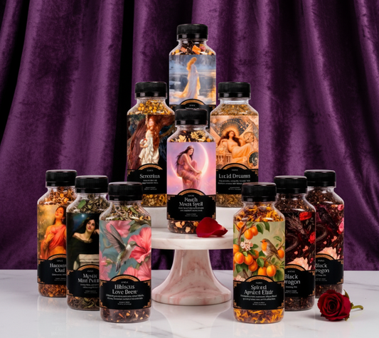 A collection of ten decorative bottles of essential oils and body scrubs arranged on a white marble pedestal against a white background. The bottles feature artistic illustrations of classical figures, fruits, and spices, and are topped with black caps.
