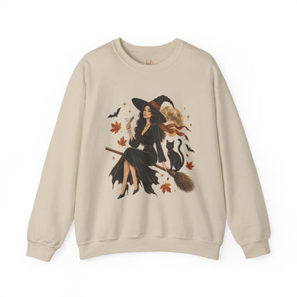 A beige crewneck sweatshirt featuring a large graphic print of a witch riding a broomstick with a black cat, surrounded by autumn leaves and bats.