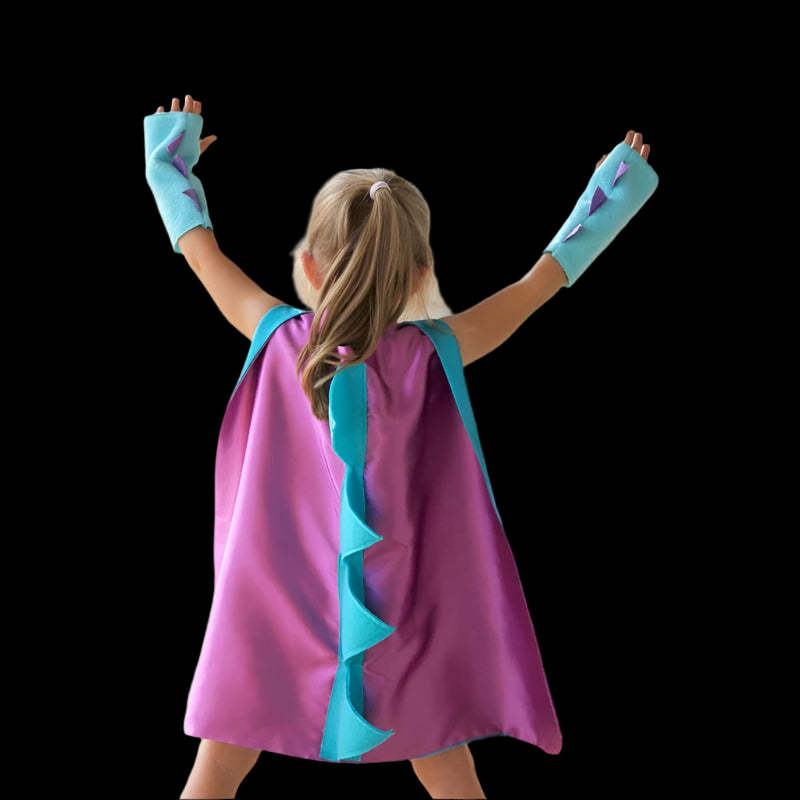 Child wearing a purple superhero cape and gloves with blue accents outdoors.