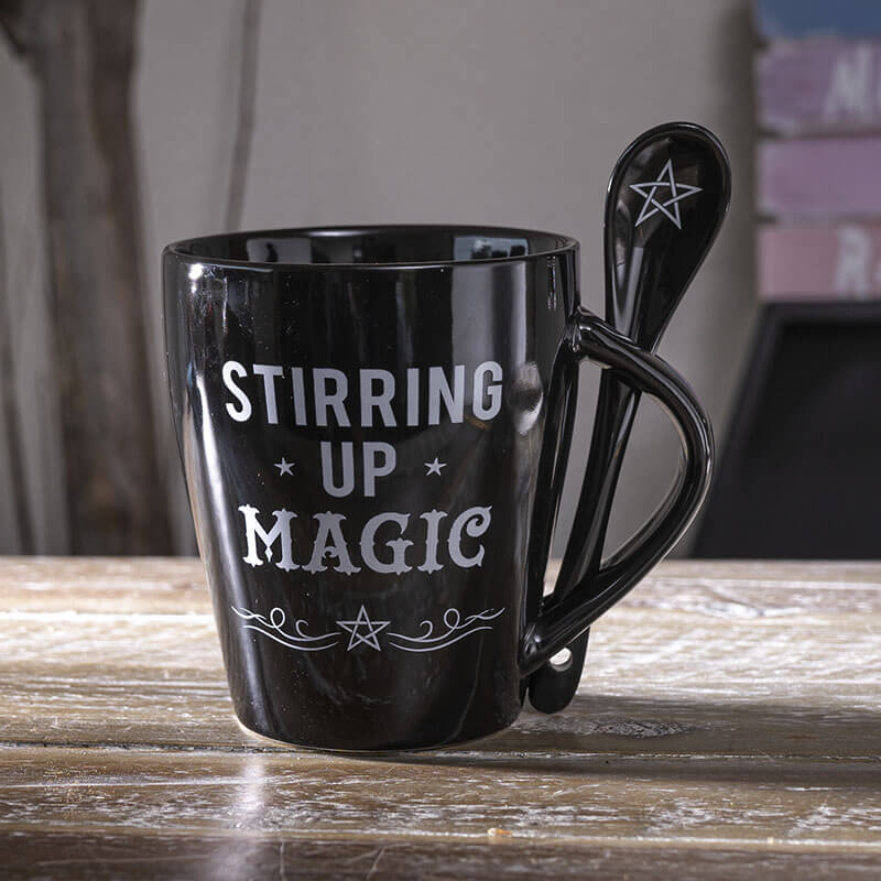 Black mug with 'Stirring Up Magic' text and a spoon on a wooden surface
