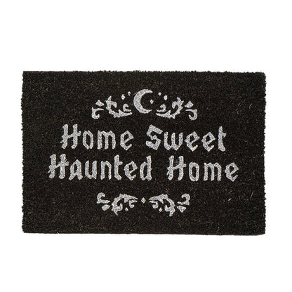 A rectangular black coir doormat with white gothic-style text reading 'Home Sweet Haunted Home' and decorative white motifs at the top and bottom, shown on a plain white background.