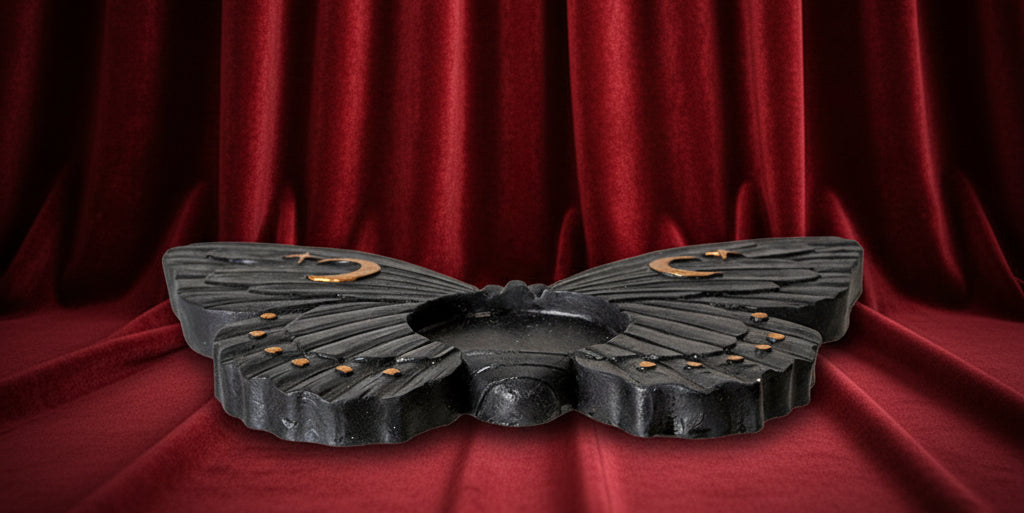 A black butterfly-shaped decorative object with small gold crescent moon and dot details on the wings, shown against a plain white background.