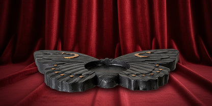 A black butterfly-shaped decorative object with small gold crescent moon and dot details on the wings, shown against a plain white background.