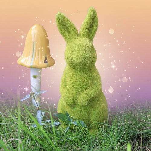 Green mossy rabbit figurine and yellow mushroom in a natural setting with grass and woodpile.