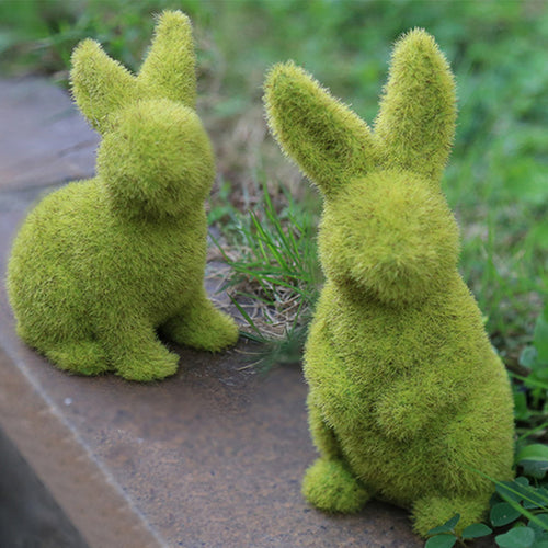 Two moss-covered rabbit sculptures on a stone surface with grass in the background