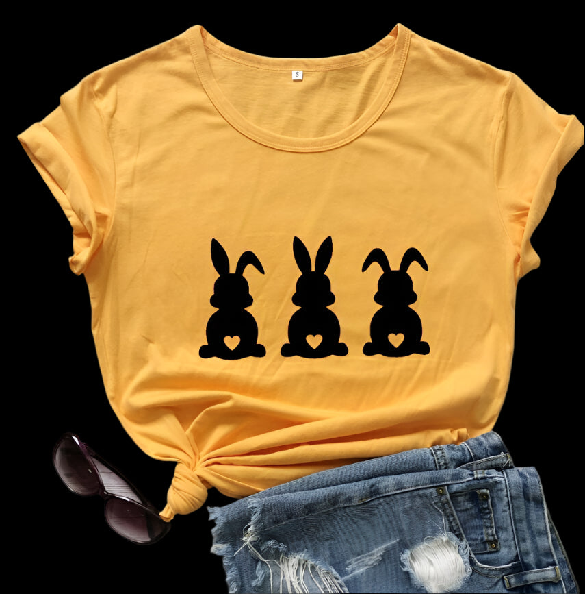 Yellow t-shirt with black rabbit silhouettes on a wooden surface with sunglasses and jeans.