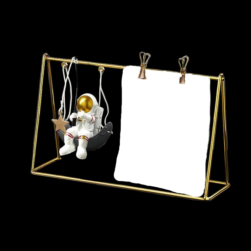 Gold metal frame holding a calendar and small figurine on a dark surface with a gray background