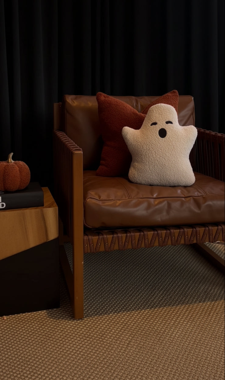 Brown leather chair with a ghost-shaped pillow and pumpkin decoration in a room.