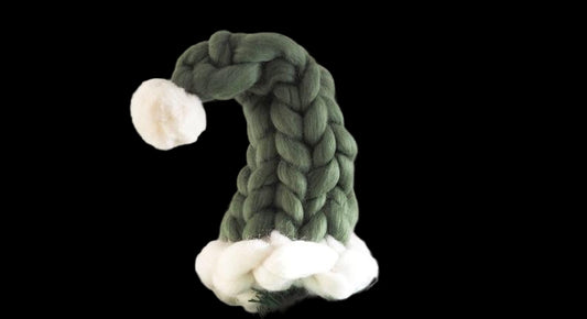 Green braided gnome hat on a small Christmas tree with a white background