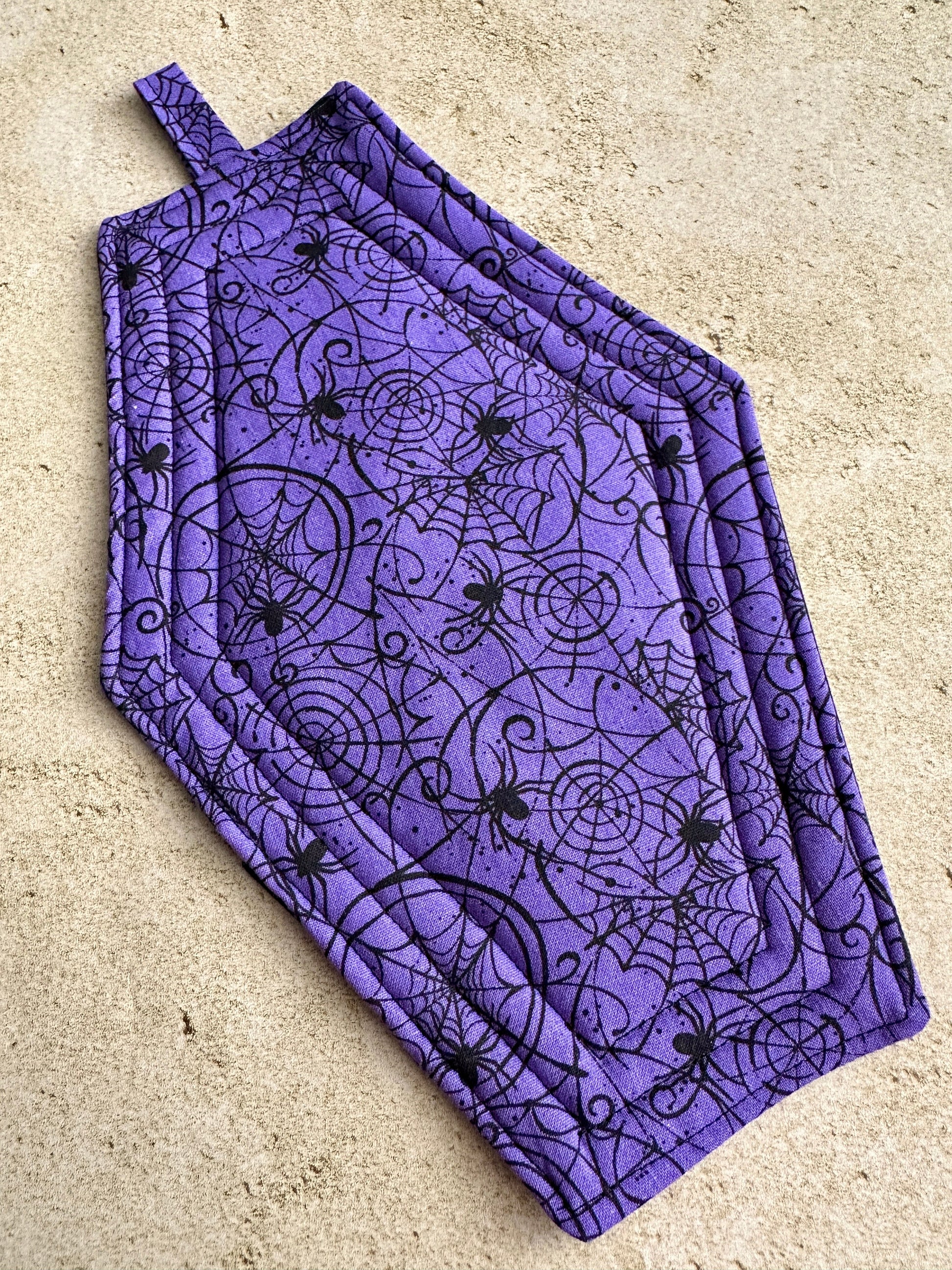 Purple apron with black spider and web pattern on a beige surface