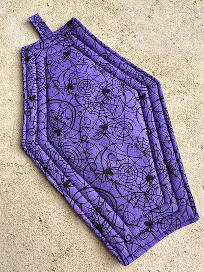 Purple apron with black spider and web pattern on a beige surface