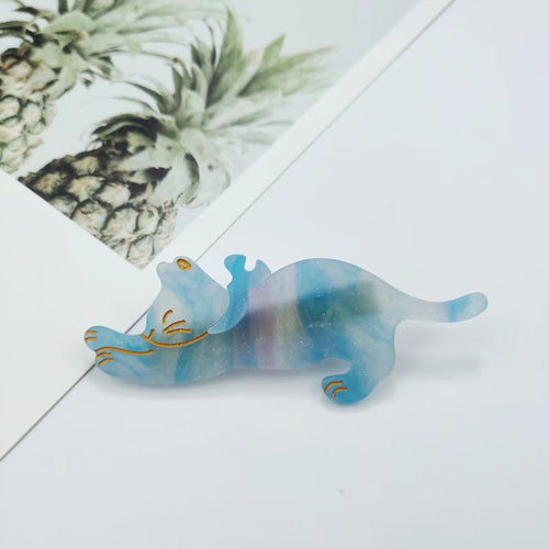 Marbled blue and green cat-shaped object on a white surface with a pineapple-themed card in the background.