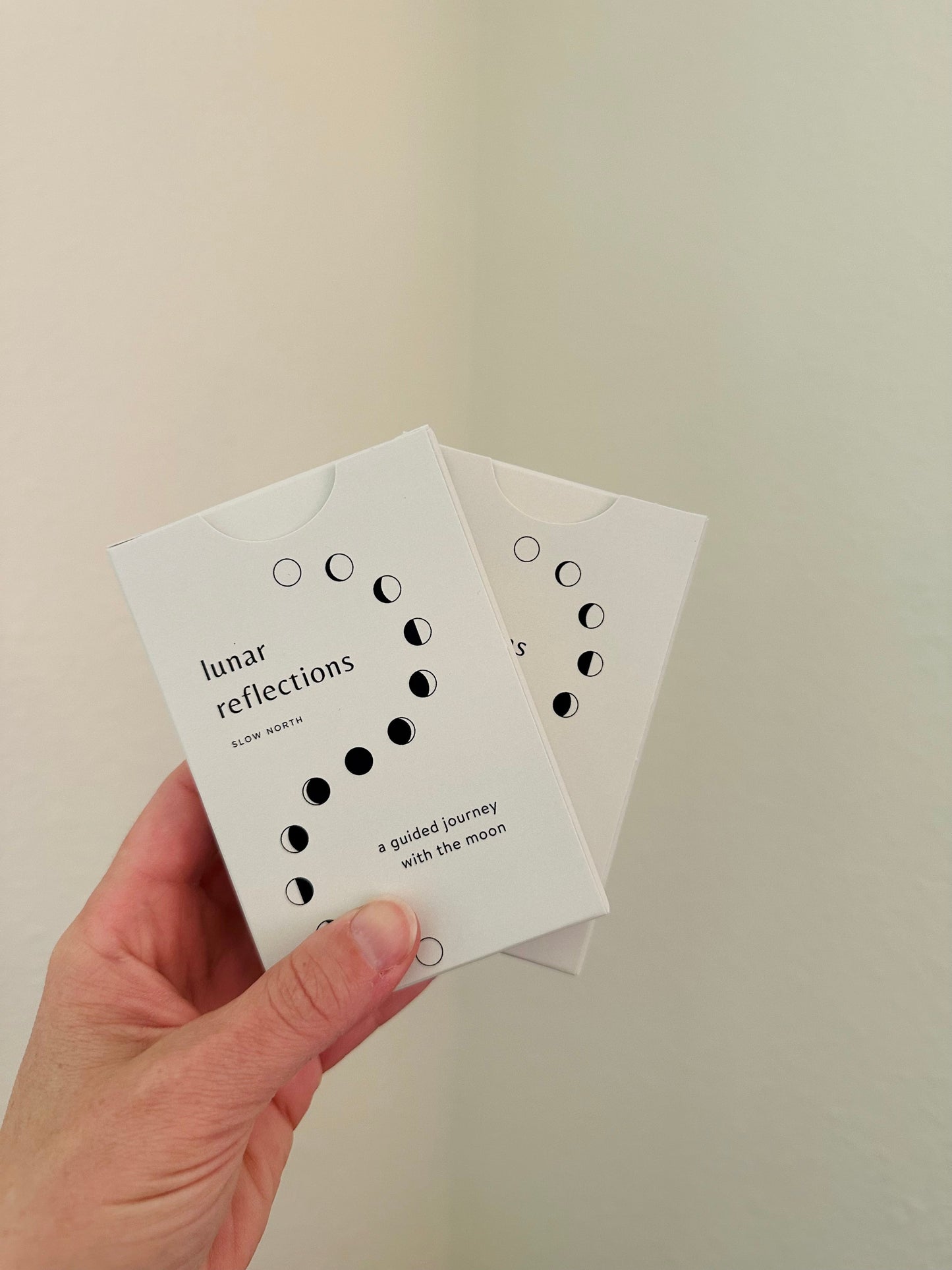 Hand holding a card with 'lunar reflections' text against a plain background