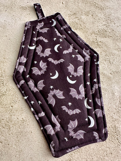 Set of two dark purple pot holders with bat and moon pattern on a concrete surface