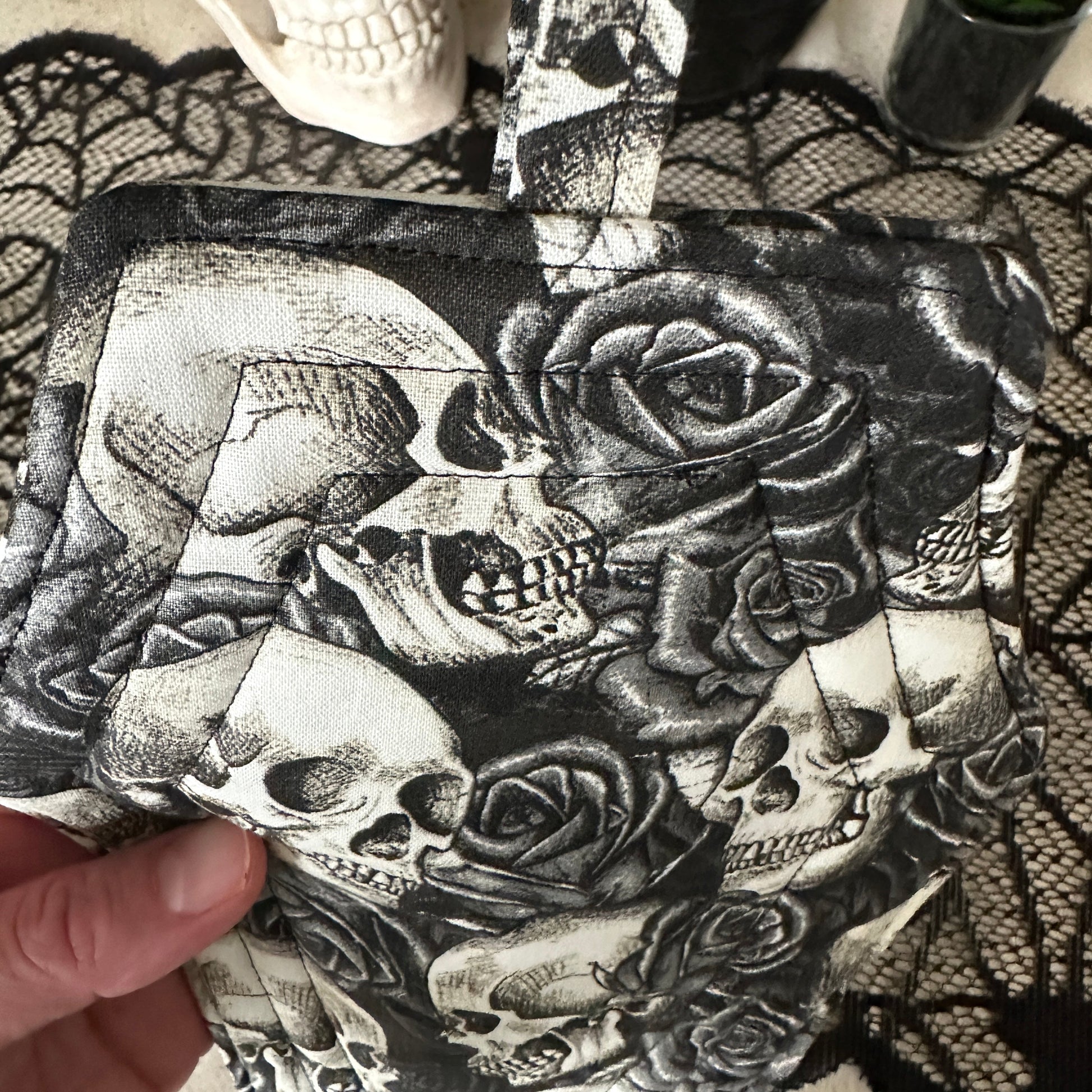 Handbag with skull and rose design held by a hand on a black lace background