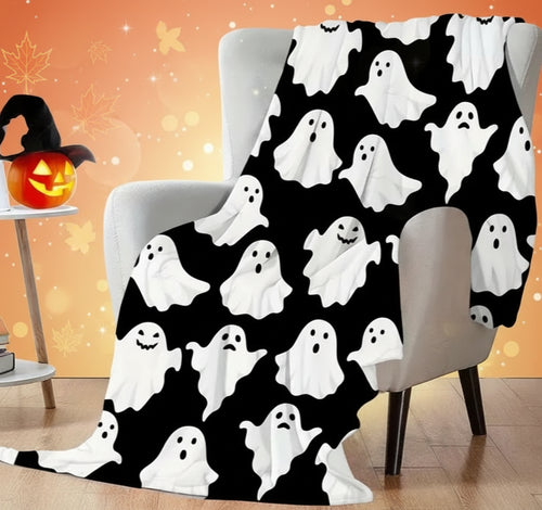 Halloween-themed ghost pattern blanket draped over a chair in a room with a pumpkin and books.