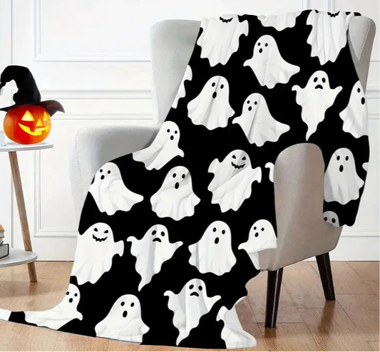 Halloween-themed ghost pattern blanket draped over a chair in a room with a pumpkin and books.