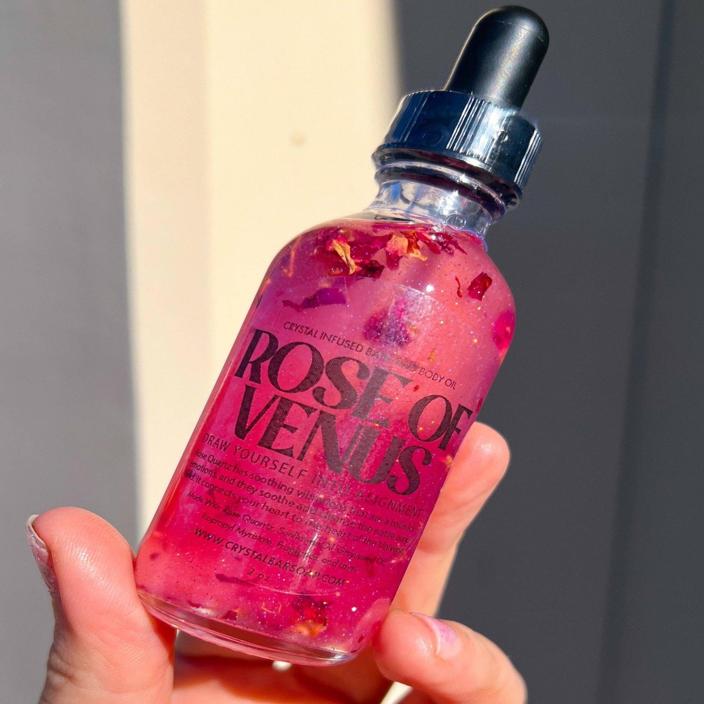 Bottle of 'Rose of Venus' with a dropper held in a hand against a neutral background