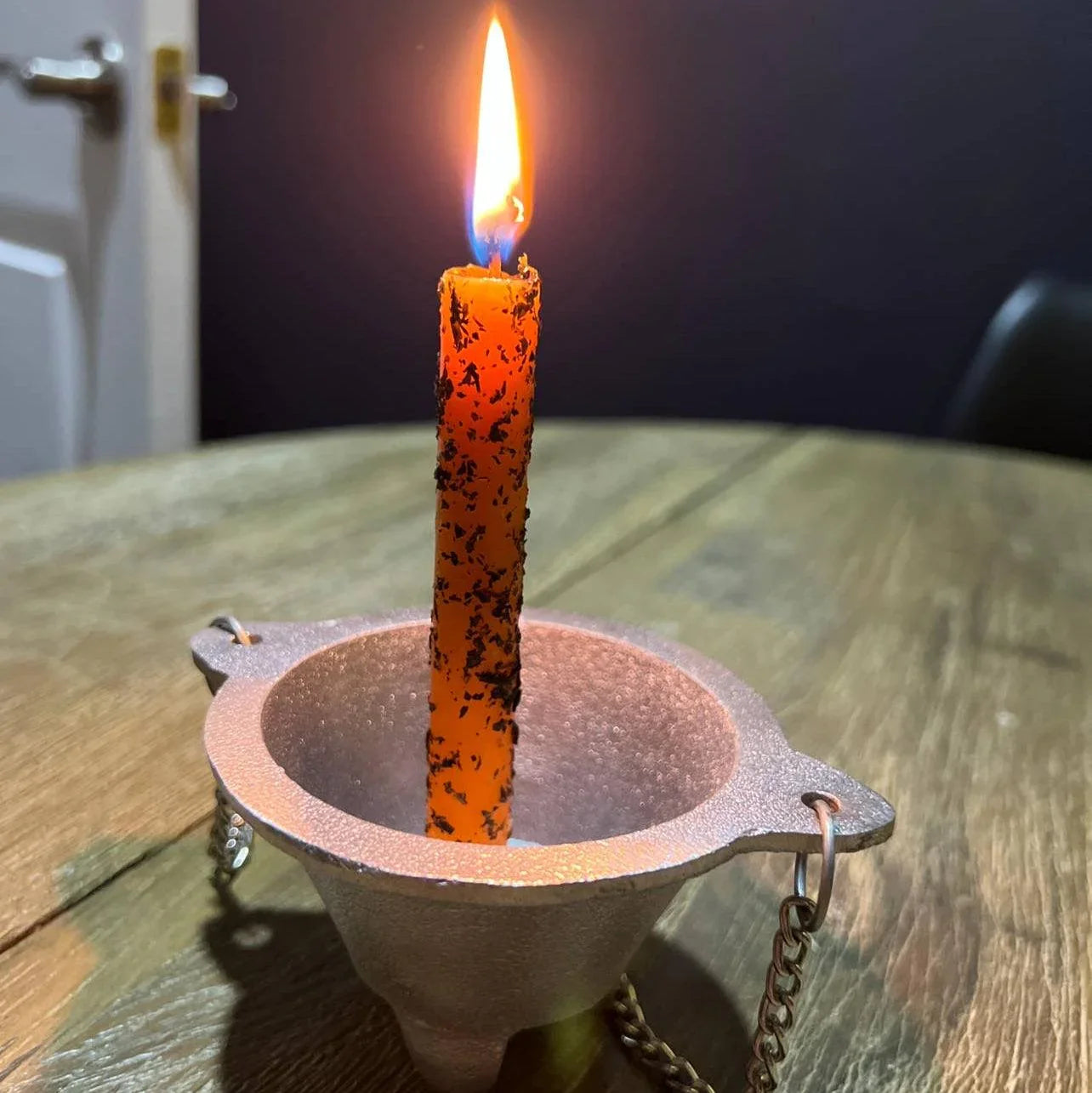 Orange candle in a metal holder on a wooden surface with a dark background