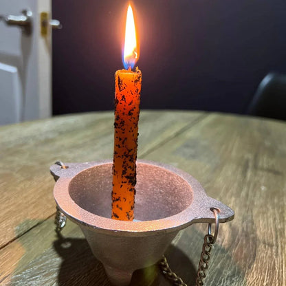 Orange candle in a metal holder on a wooden surface with a dark background