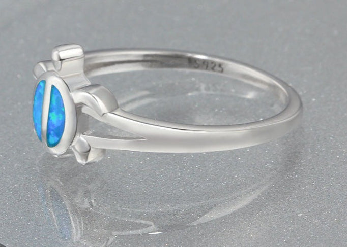 Silver ring with a blue opal stone on a reflective surface