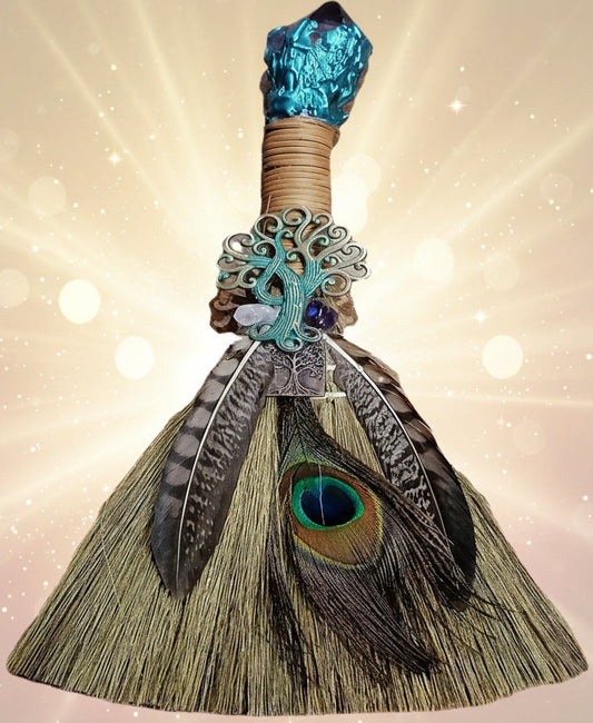 Decorative broom with peacock feathers and turquoise accents on a white background