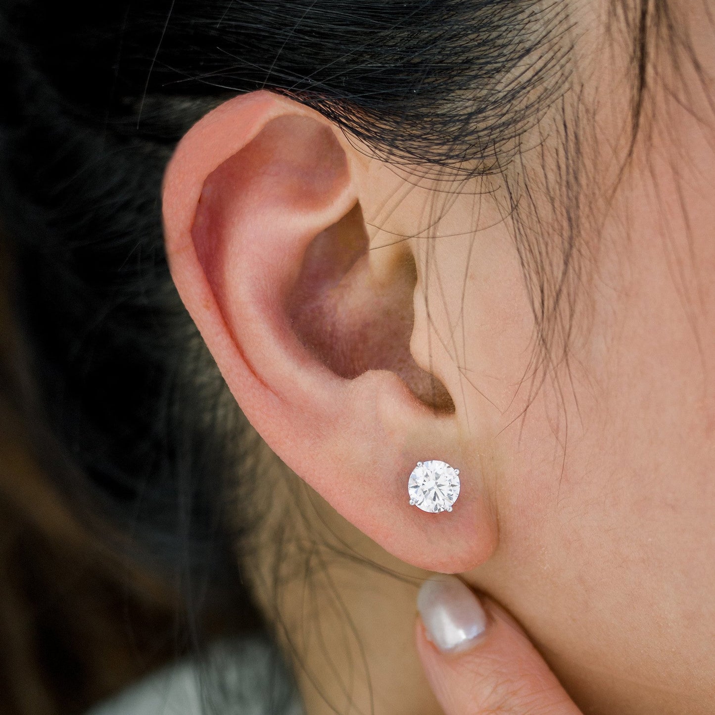 Close-up of an ear wearing a diamond stud earring with blurred background