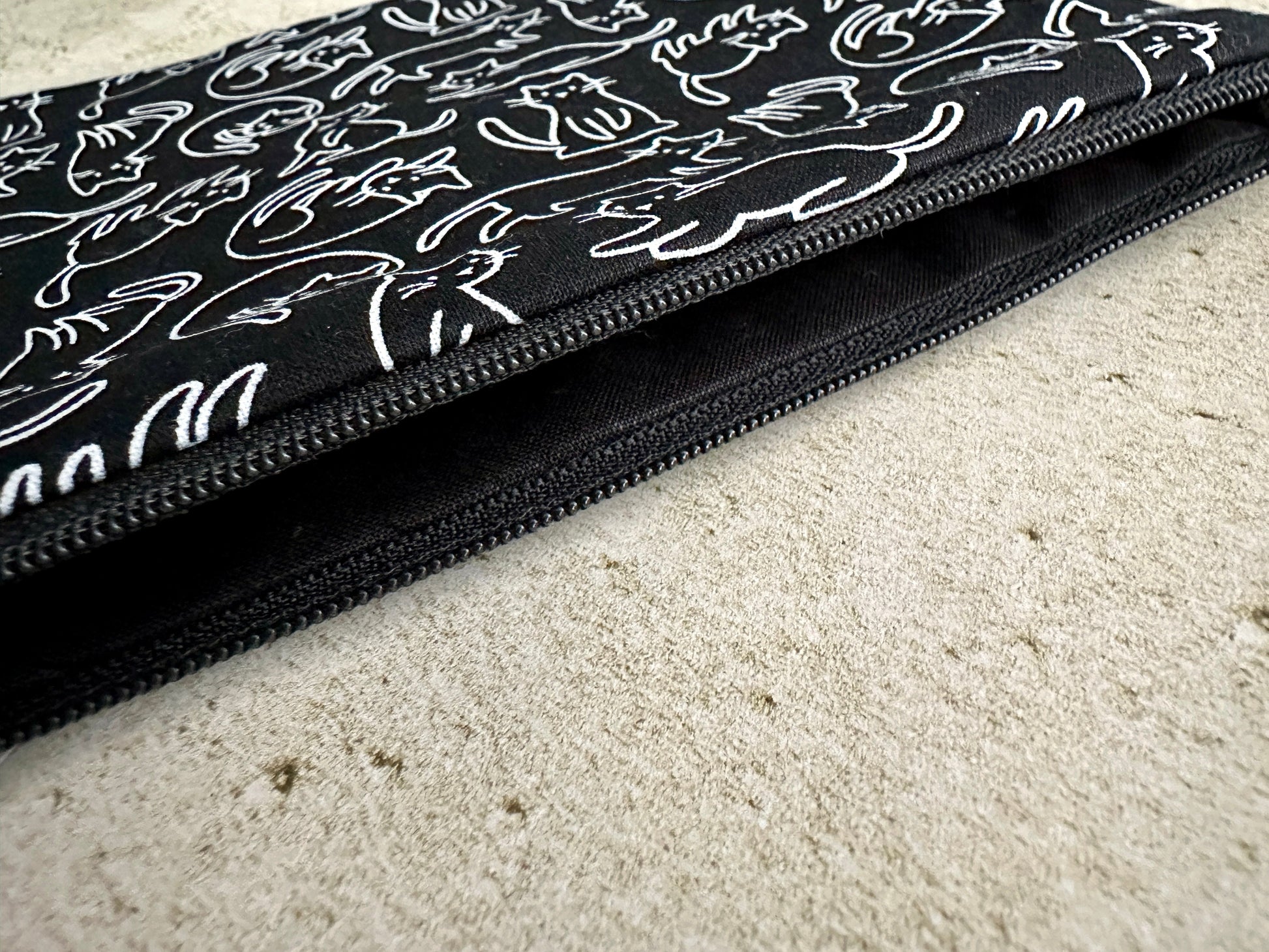 Black pouch with white cat pattern on a beige surface